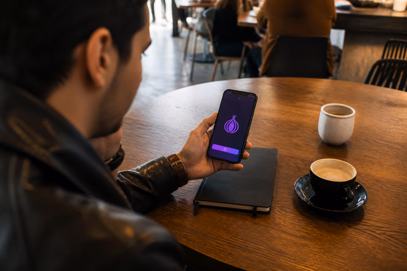 A person using Onion Browser on an iPhone in a cozy café, illustrating safe dark web access.